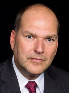 Porträt Michael Ruck mit ernstem Blick im Anzug und dunklem Hintergrund.